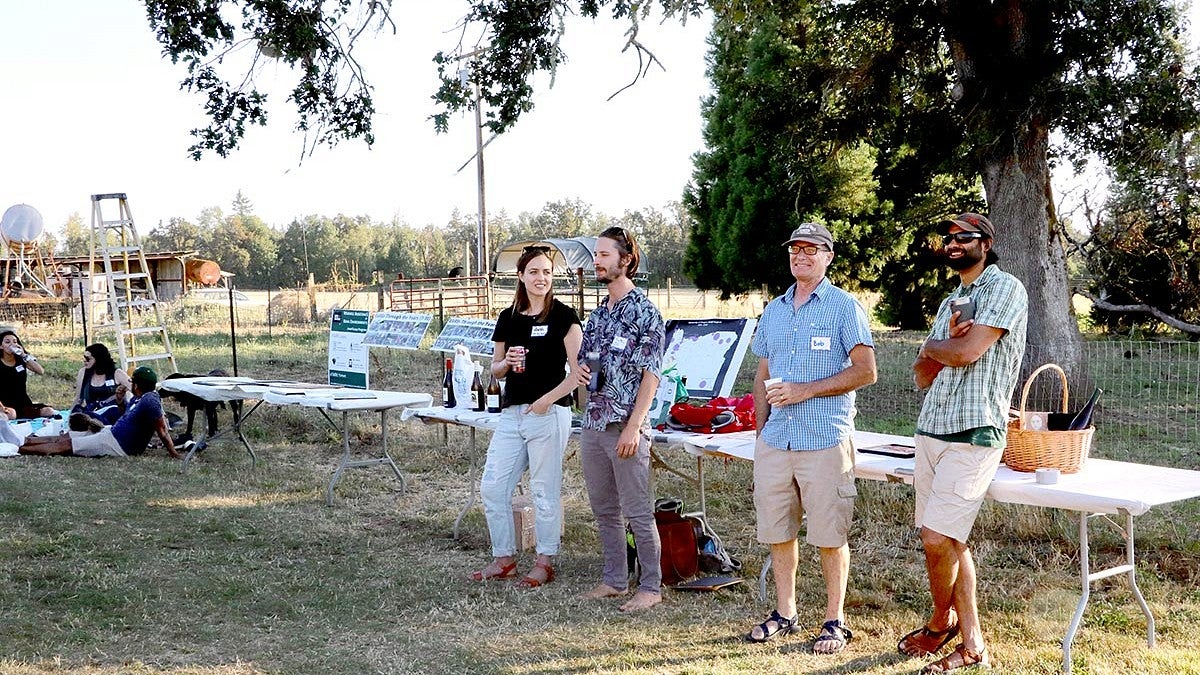 four people standing in front of a table outside in the grass