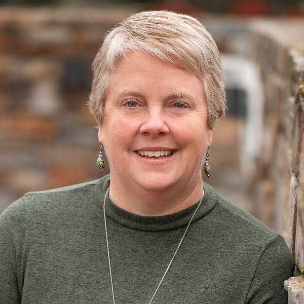 Photograph of a woman with cropped hair in front of a blurred object. 