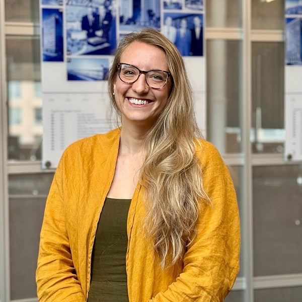 Photograph of a smiling woman in yellow with long hair and glasses. 